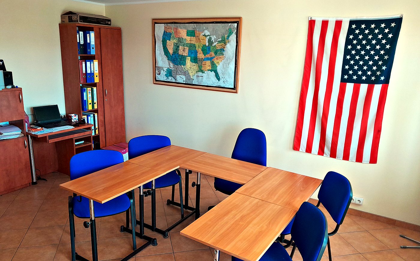 Sala AcCentu: mapa Stanów Zjednoczonych i amerykańska flaga nad stołami z niebieskimi krzesłami